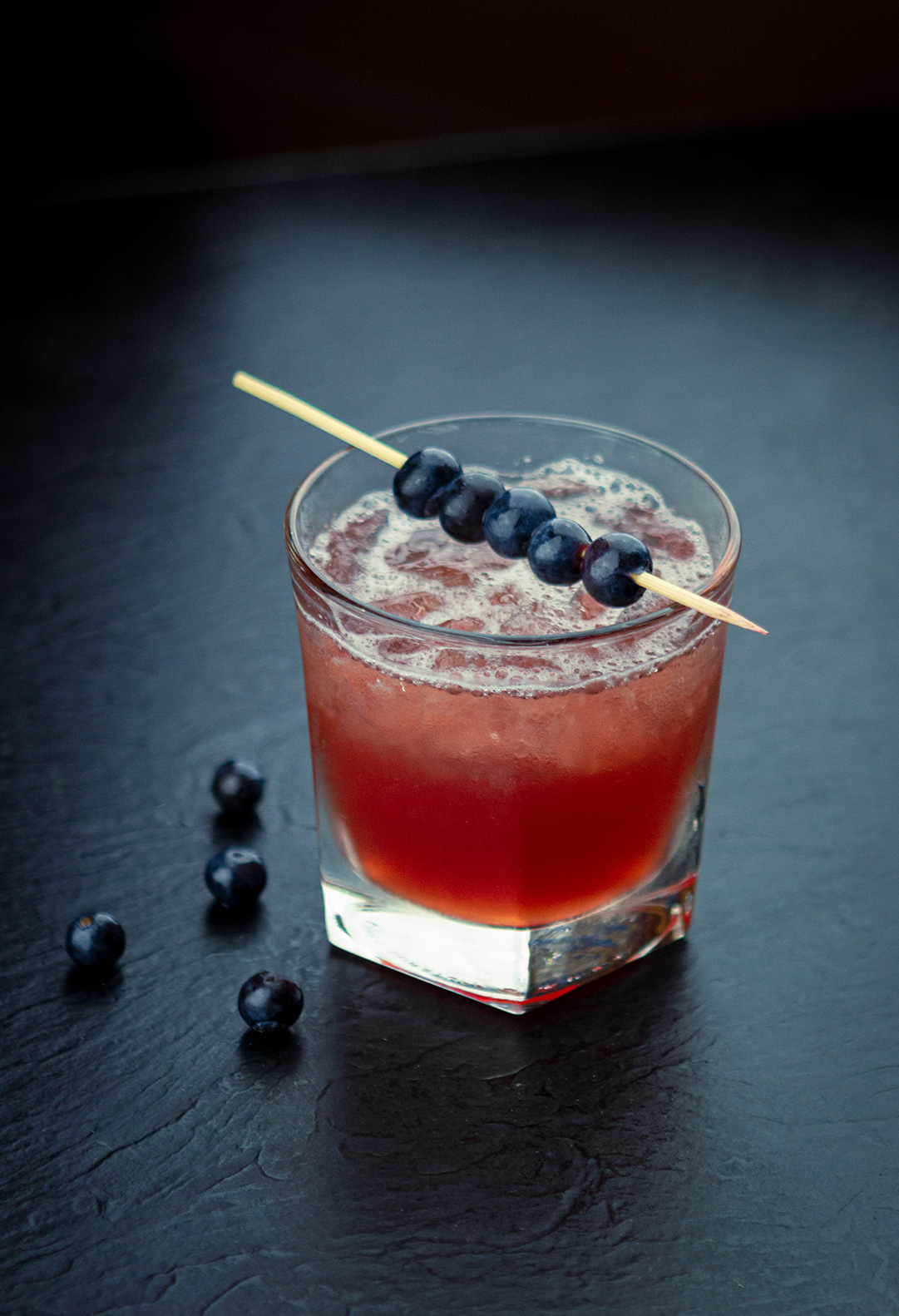 Blueberry cocktail with blue berries next to glass
